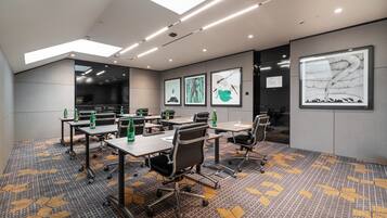 A modern conference room with a high ceiling, recessed lighting, and a patterned carpet.