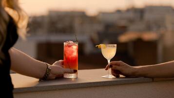 Two people holding drinks at a bar with a cityscape view in the background.