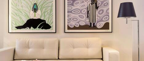 Una sala de estar moderna con un sofá blanco, una mesa de centro de vidrio con revistas, un jarrón con flores y dos cuadros en la pared.