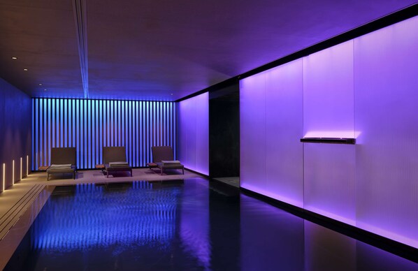 Un moderno cuarto de spa con piso reflectante, dos sillones de descanso e iluminación vertical en la pared.