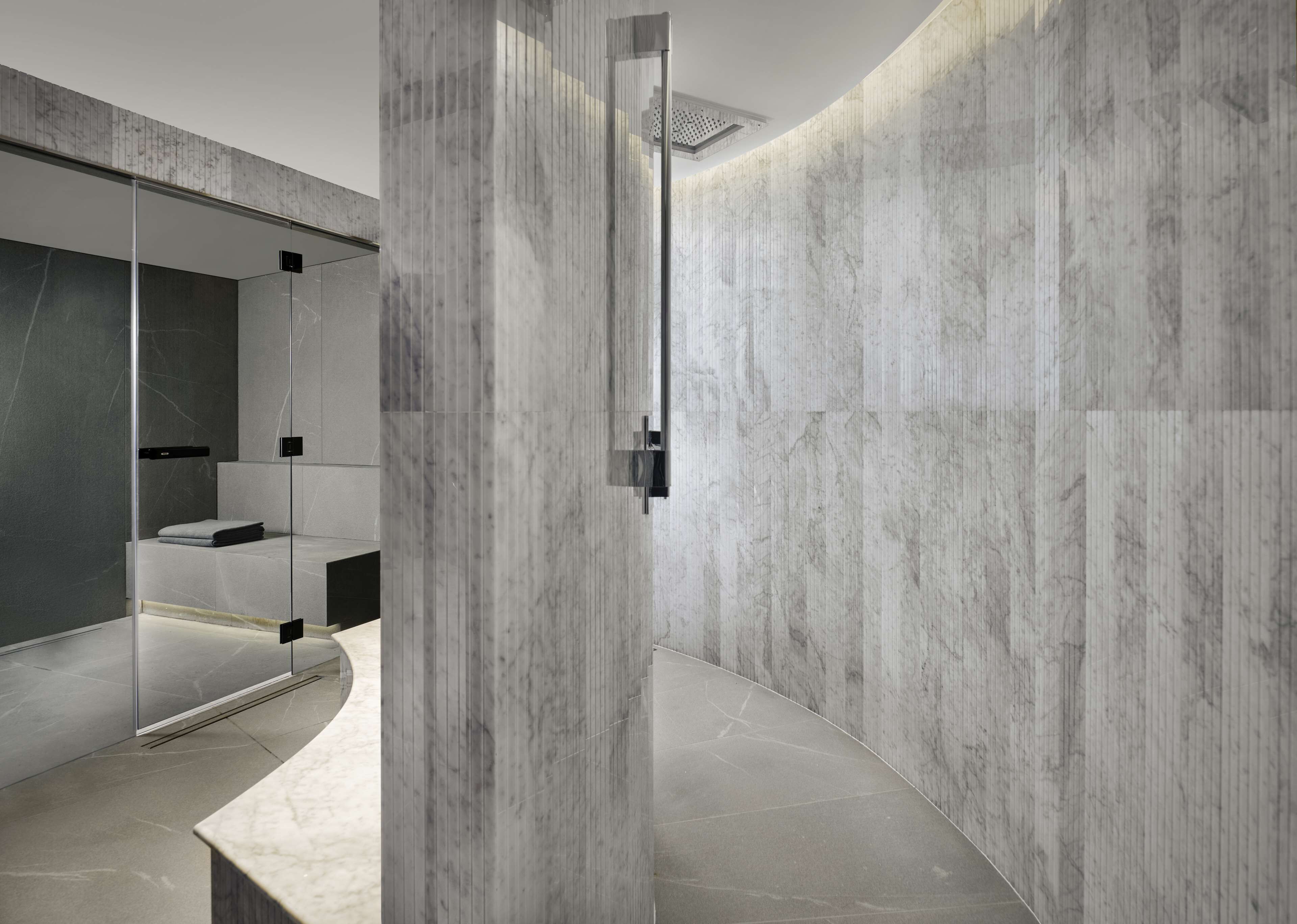 Un baño moderno con paredes de mármol, cabina de ducha de vidrio y diseño minimalista.