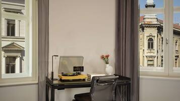 A room with a desk, a chair, a computer, a vase with flowers, and a view of a historic building.