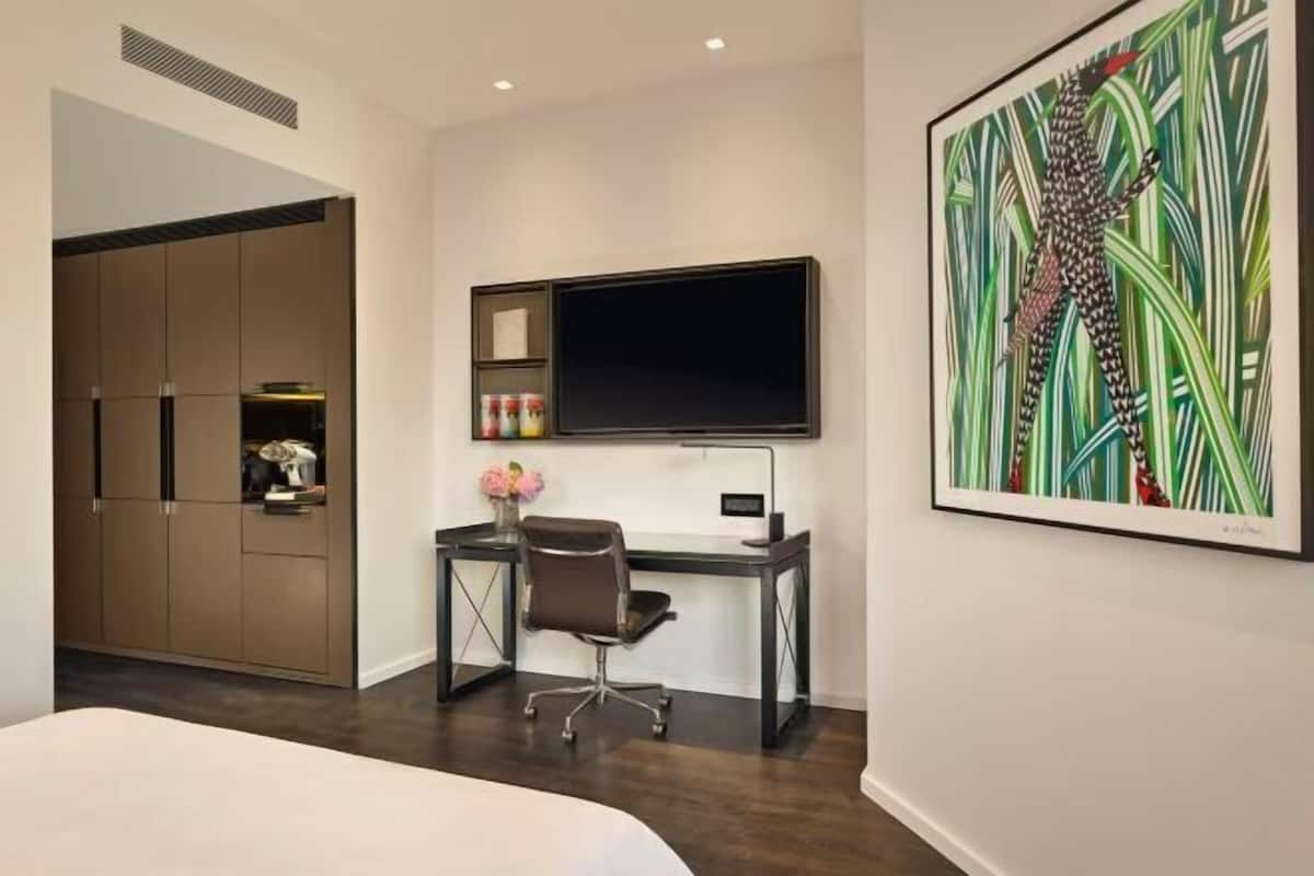 Une chambre d’hôtel comprenant un lit, un bureau avec un ordinateur, une télévision, une armoire et un grand tableau abstrait accroché au mur.