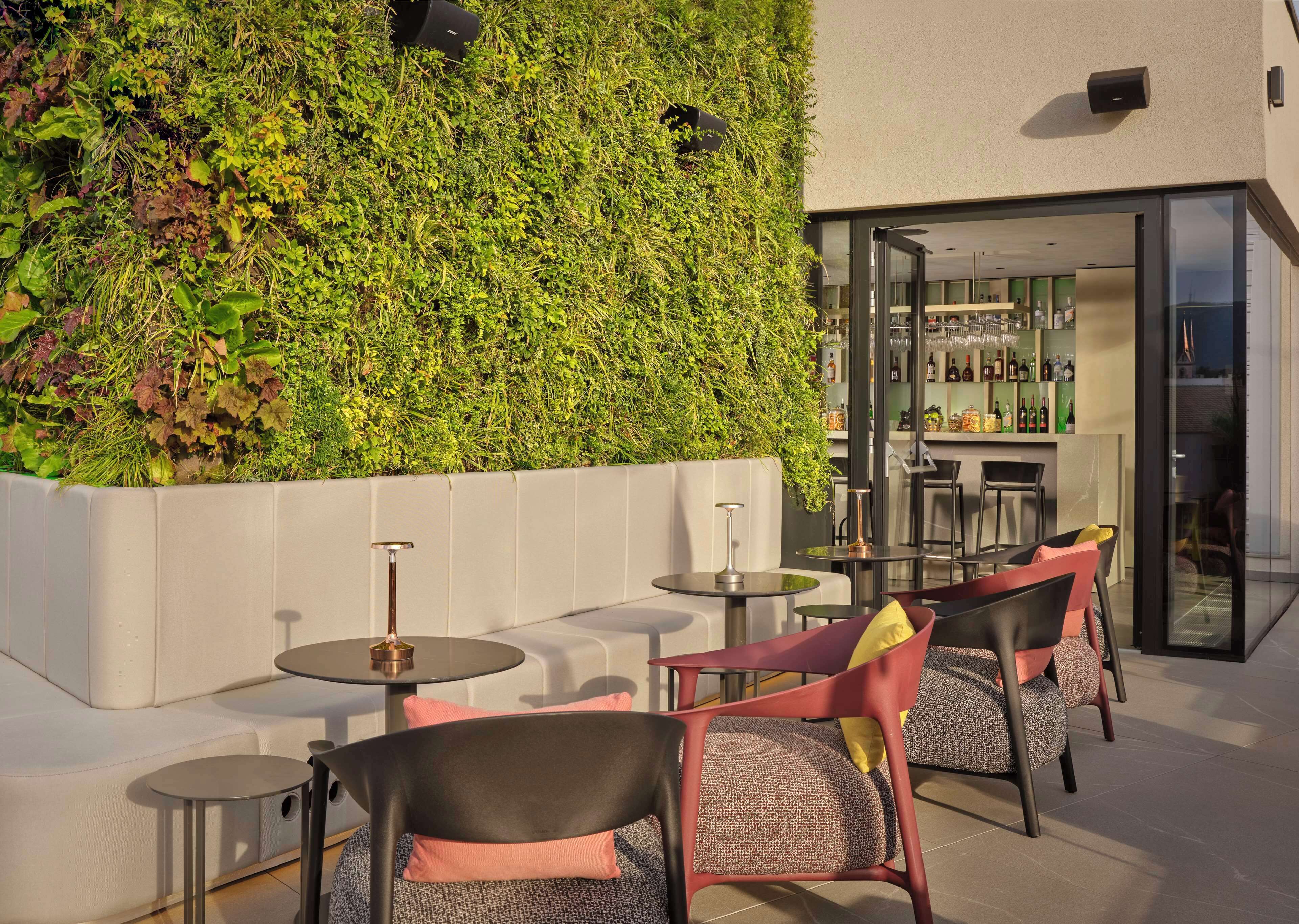 Un área de estar al aire libre con muebles modernos, una barra con diversas botellas y una pared verde con plantas.