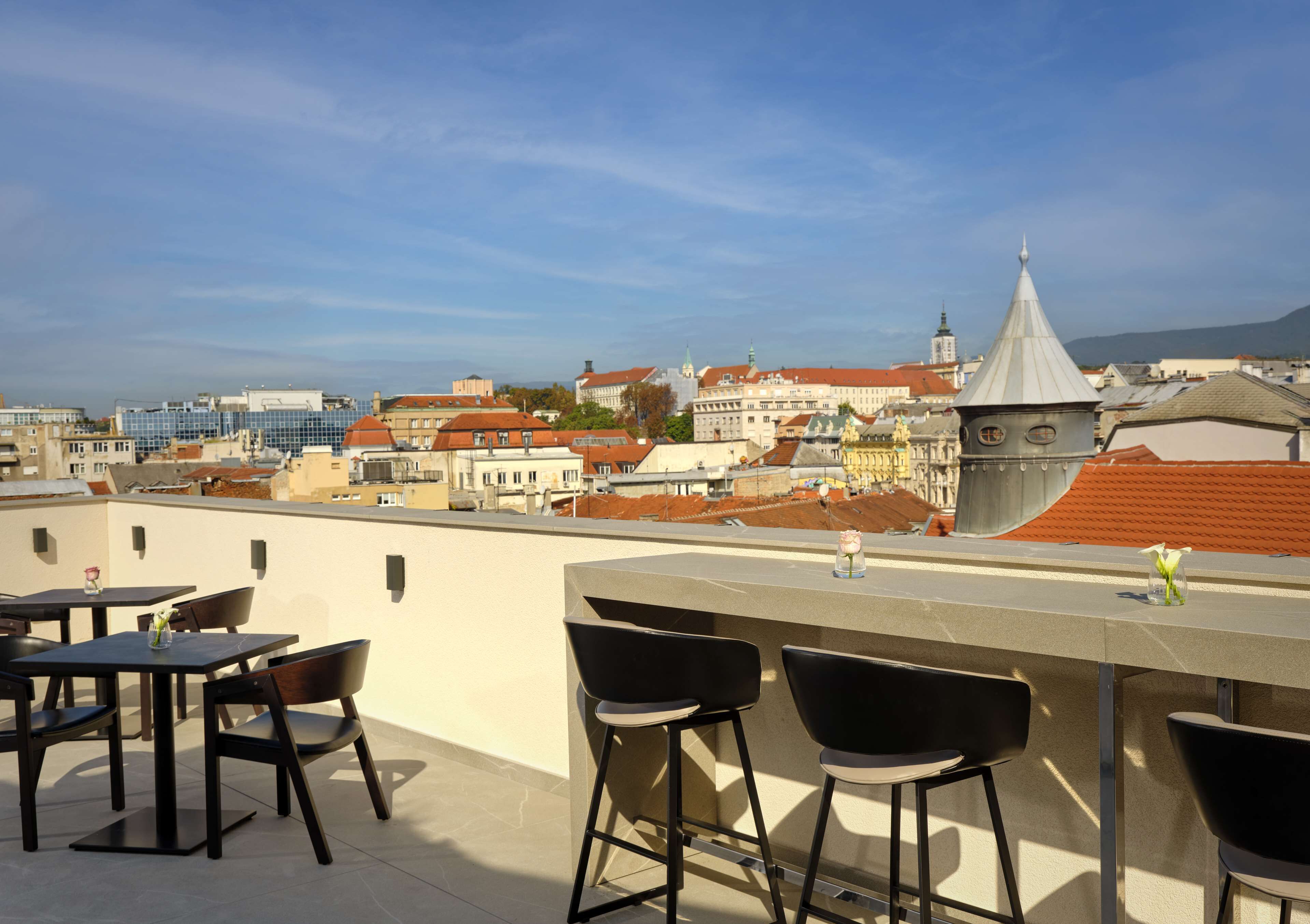 Una terraza en la azotea con zona de bar, asientos y vistas de la ciudad.