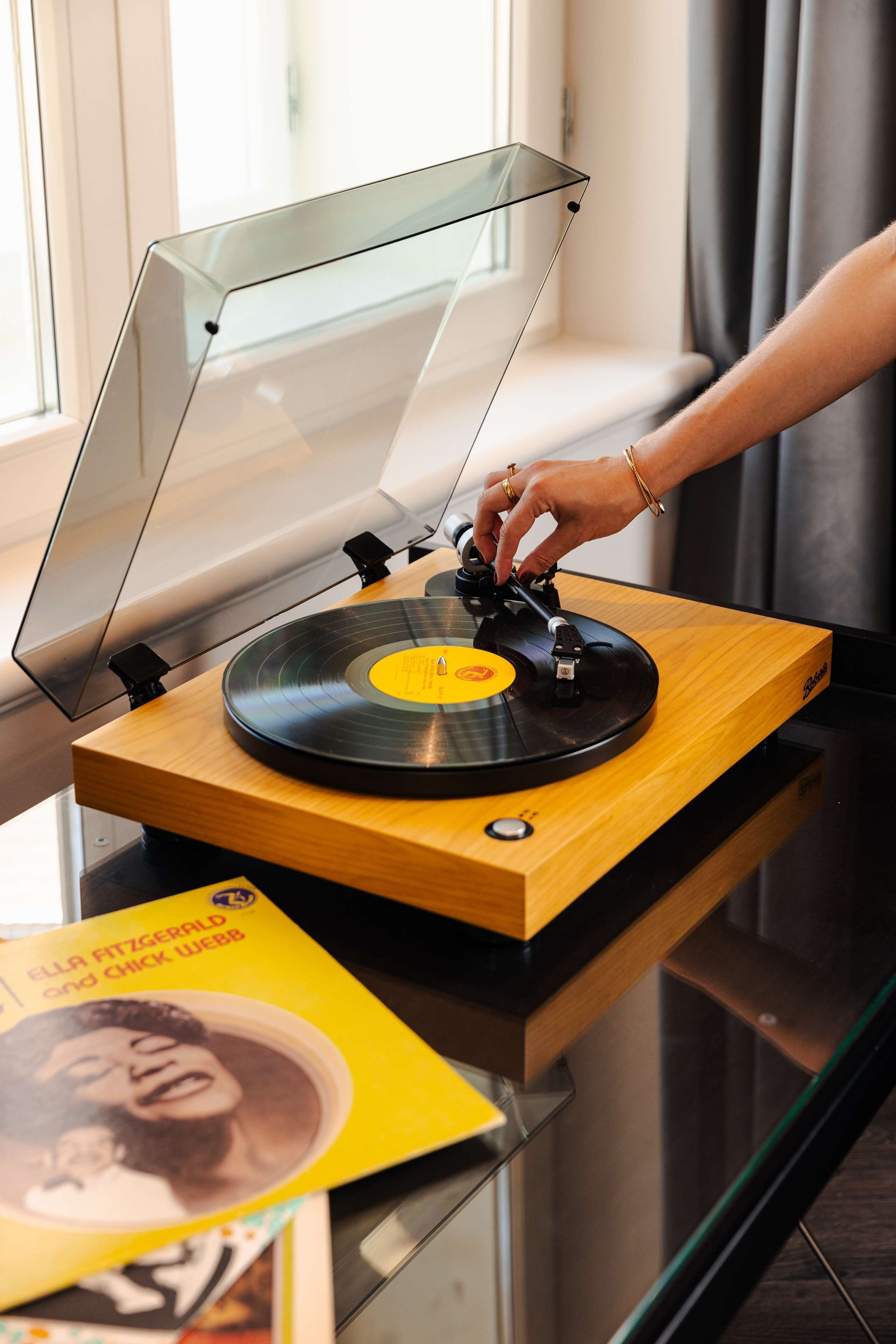 A turntable with a wooden base and a transparent cover, placed on a glass table.