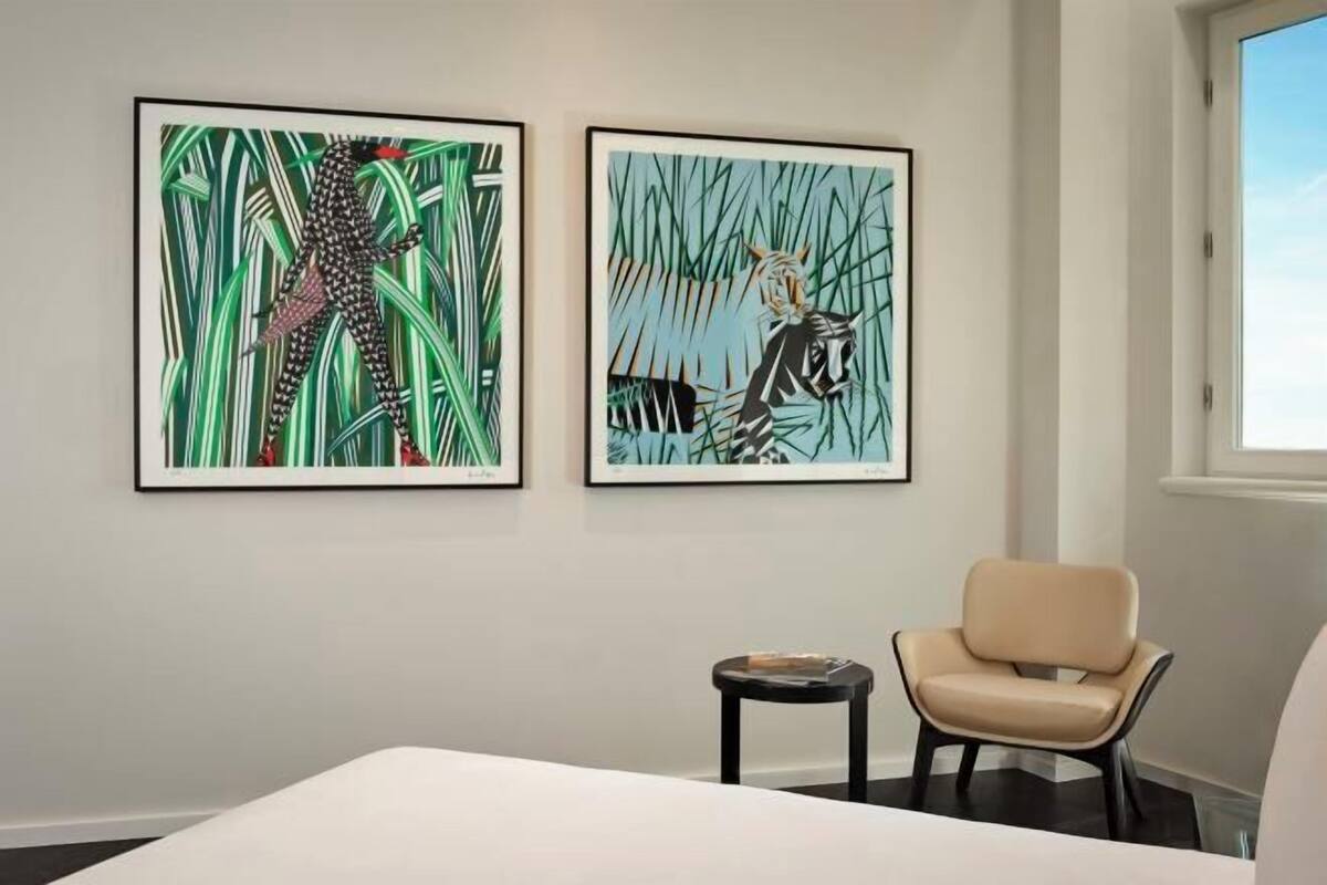 Une chambre d’hôtel avec un lit, une chaise et deux œuvres d’art encadrées accrochées au mur.