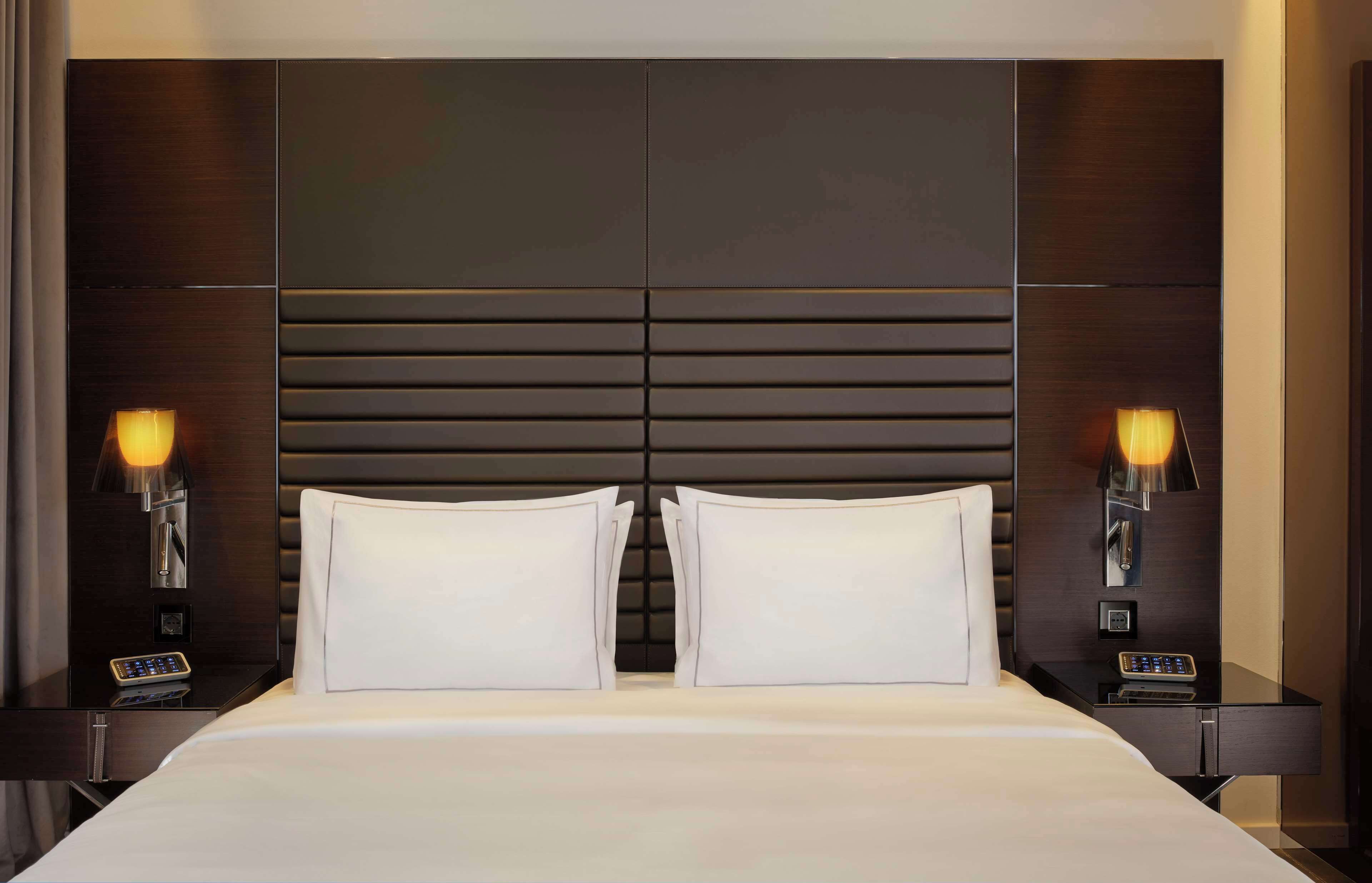 A hotel room with a large bed, two bedside tables with lamps, and a modern headboard.