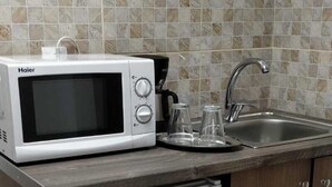 Une cuisine compacte équipée d’un micro-ondes Haier blanc, d’un petit réfrigérateur et d’un évier avec un robinet.