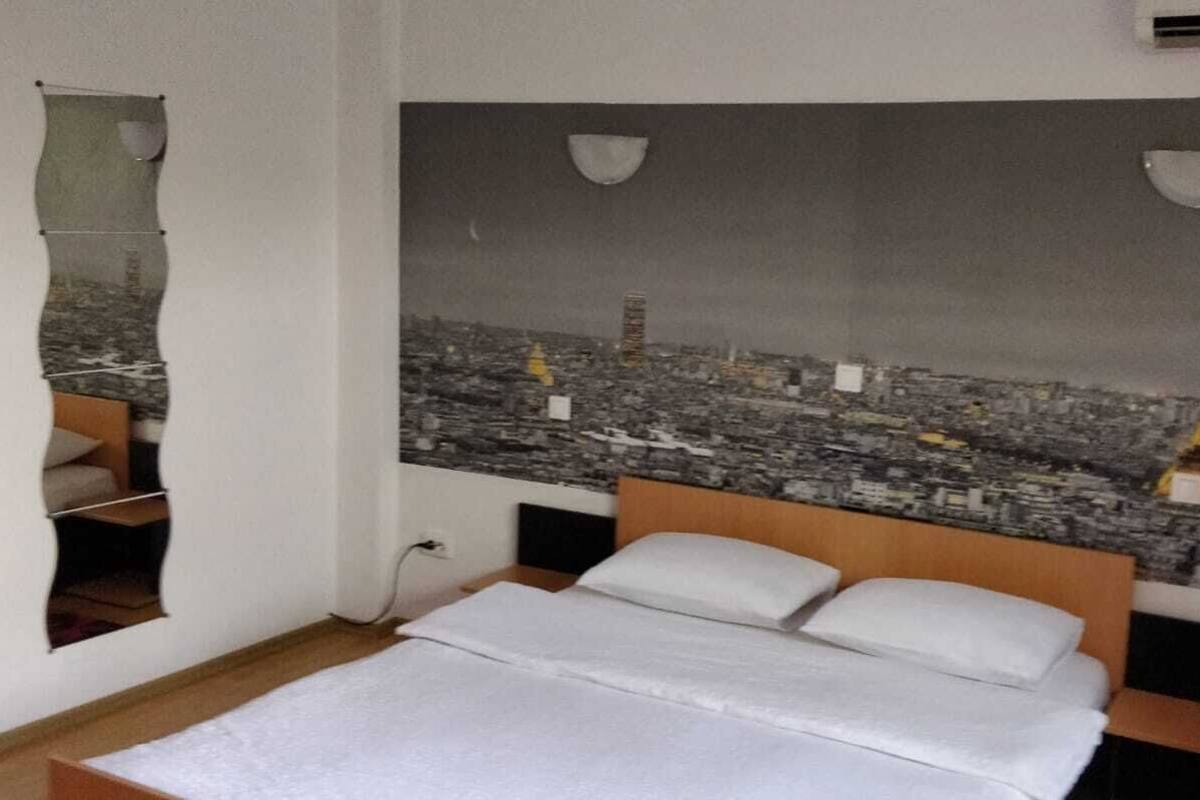 A bedroom with a bed, a wall-mounted air conditioner, and a cityscape mural featuring the Eiffel Tower.