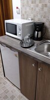 Una cocina compacta con microondas, cafetera y un lavamanos pequeño.