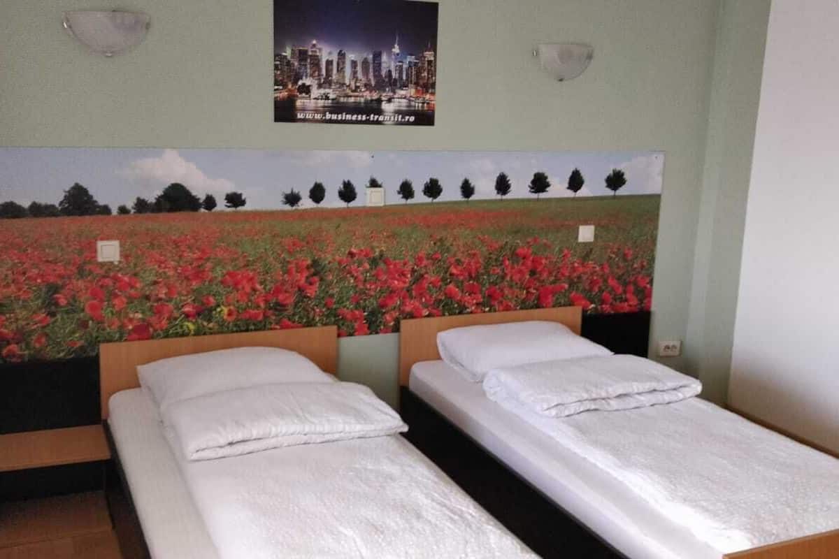 A hotel room with two beds, a cityscape poster on the wall, and a small window with a view of trees.