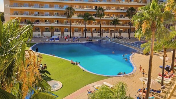 Un hotel con una piscina grande rodeada de palmeras y tumbonas.