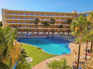 A hotel with a large swimming pool surrounded by palm trees and sun loungers.