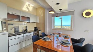 Una cocina moderna con armarios blancos, una mesa de madera para cuatro personas y vistas al mar a través de una ventana.