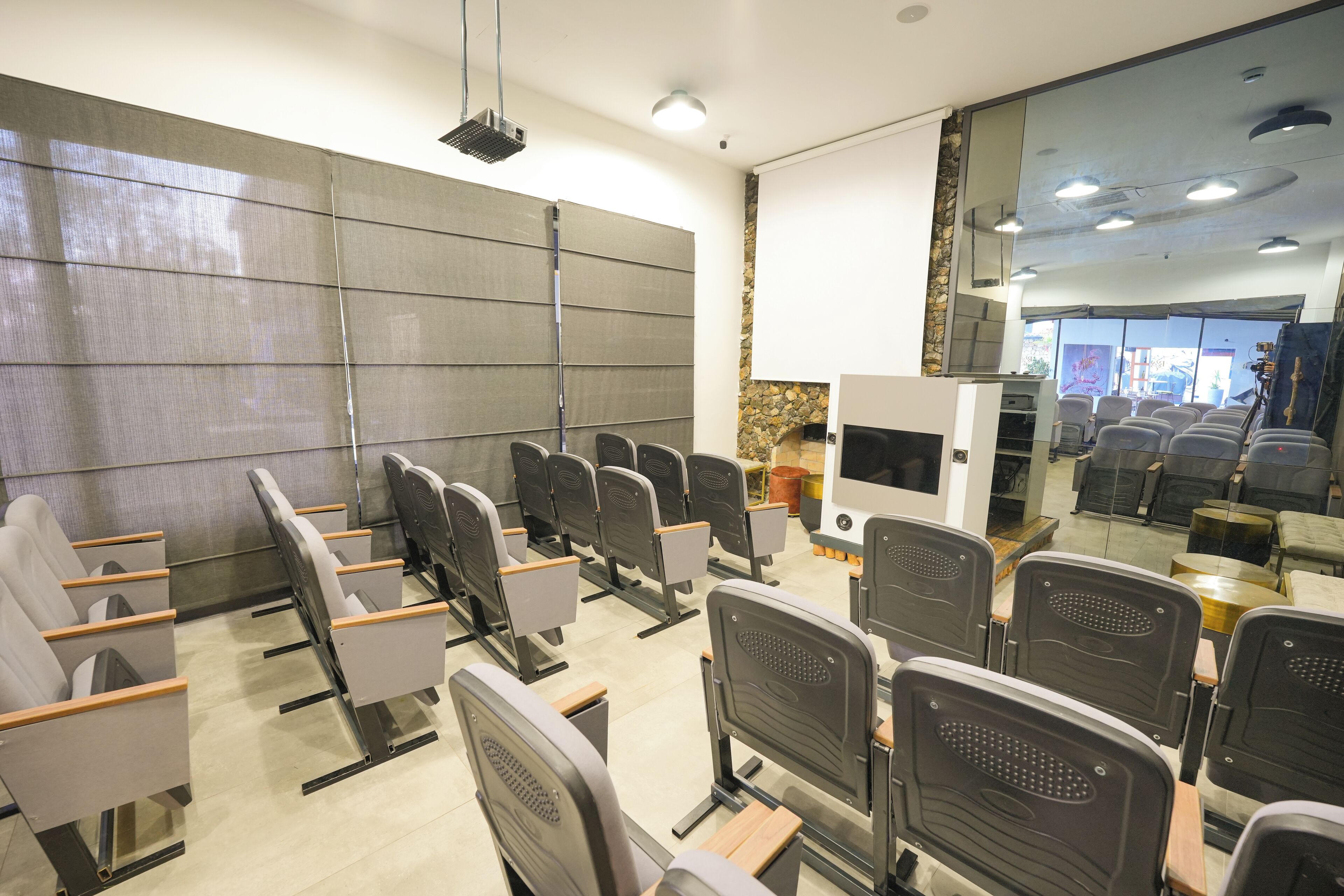 Sala de conferências com fileiras de cadeiras, um projetor e uma parede de pedra decorativa.