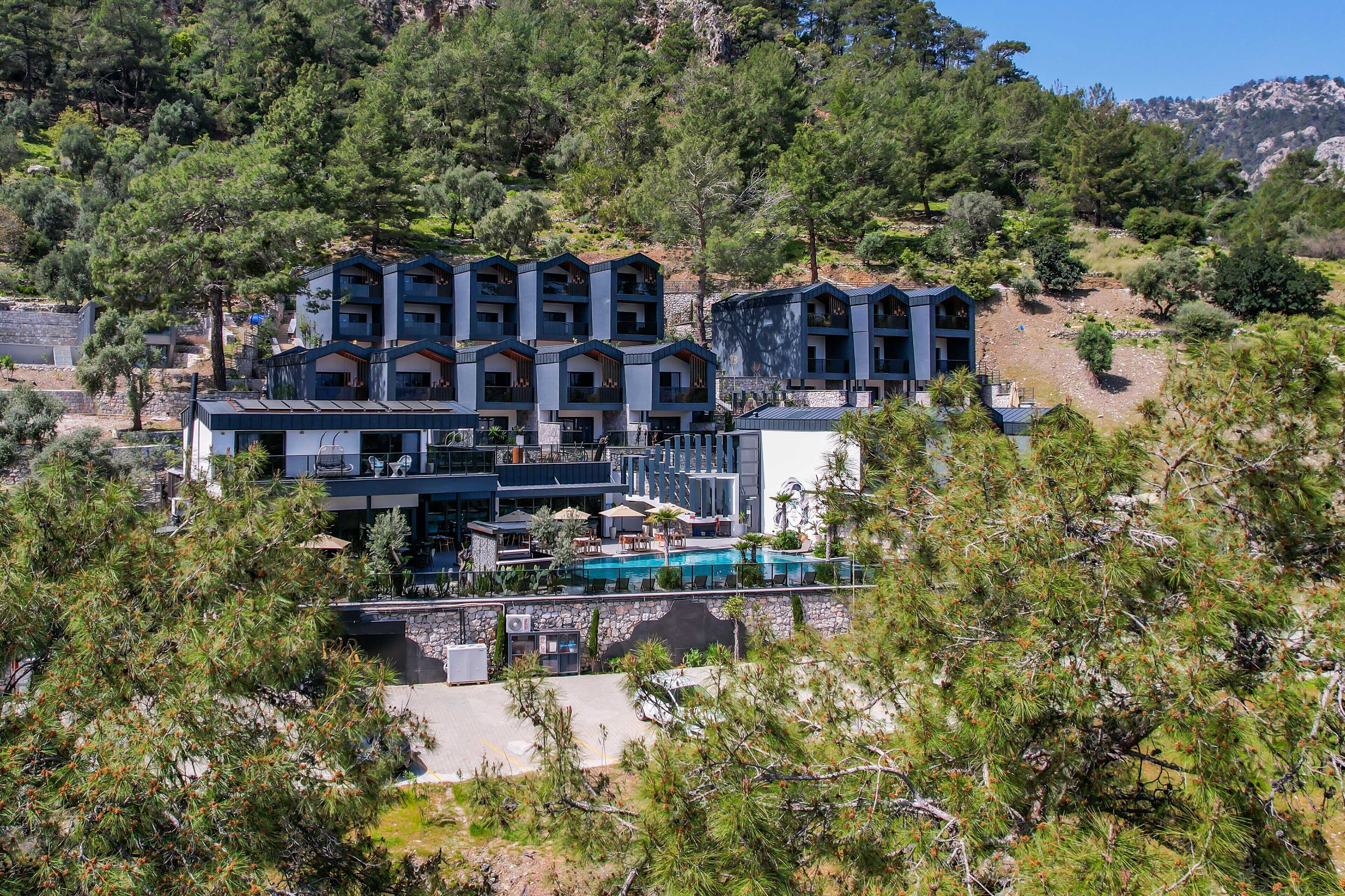 Un hotel moderno con varios balcones, una piscina y un paisaje montañoso de fondo.