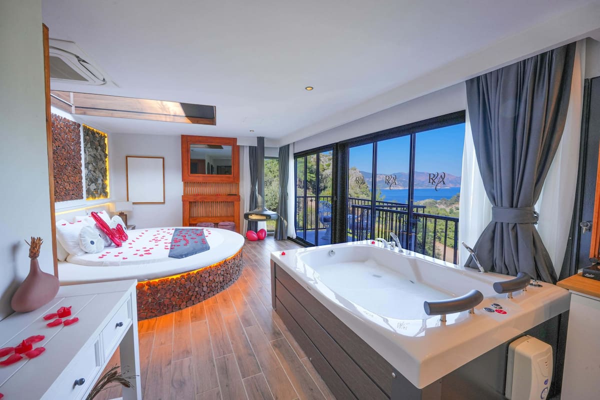 A modern bedroom with a large bed, a bathtub, and a balcony with a view of the sea.