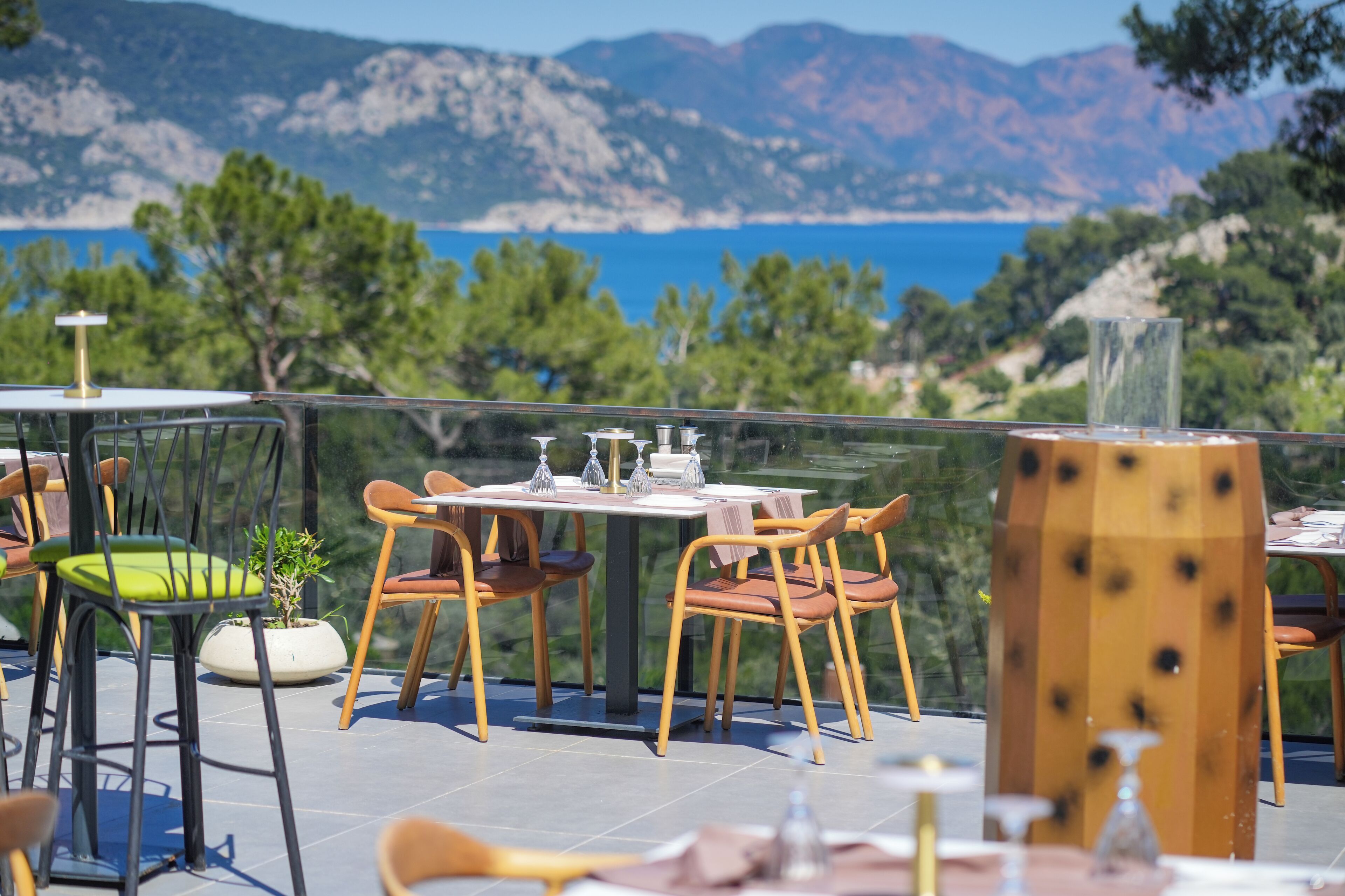 Un espace de restauration en plein air, avec des tables et des chaises, offrant une vue panoramique sur la mer et les montagnes.
