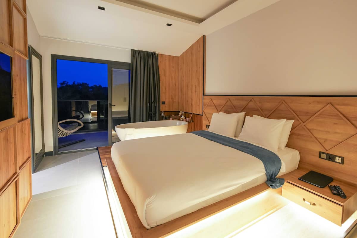 A modern hotel room with a large bed, bedside table, and a view of the outdoor area.