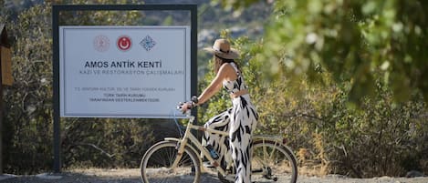 A signboard with text in a foreign language, a person wearing a hat and patterned pants, and a bicycle.