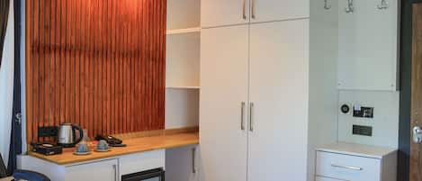 A hotel room with a kitchenette, a bed, a wardrobe, and a small fridge.