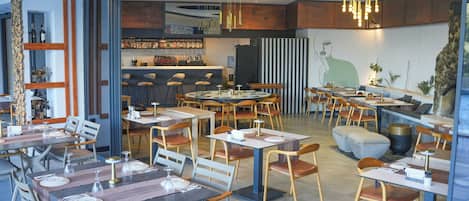 A modern restaurant with round tables, wooden chairs, and a bar area.