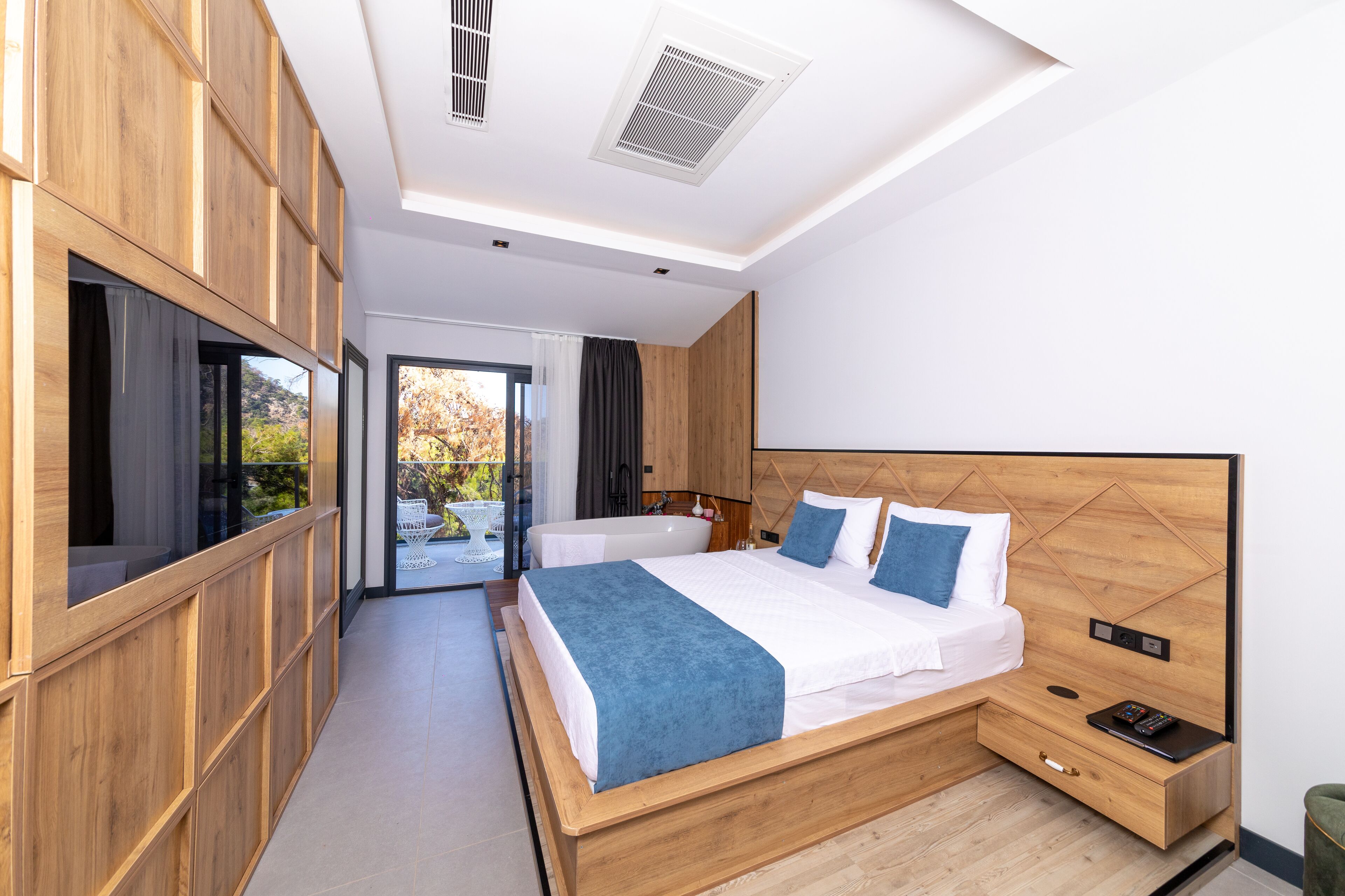 A modern bedroom with a large bed, a wooden wardrobe, and a bathroom visible through a glass door.