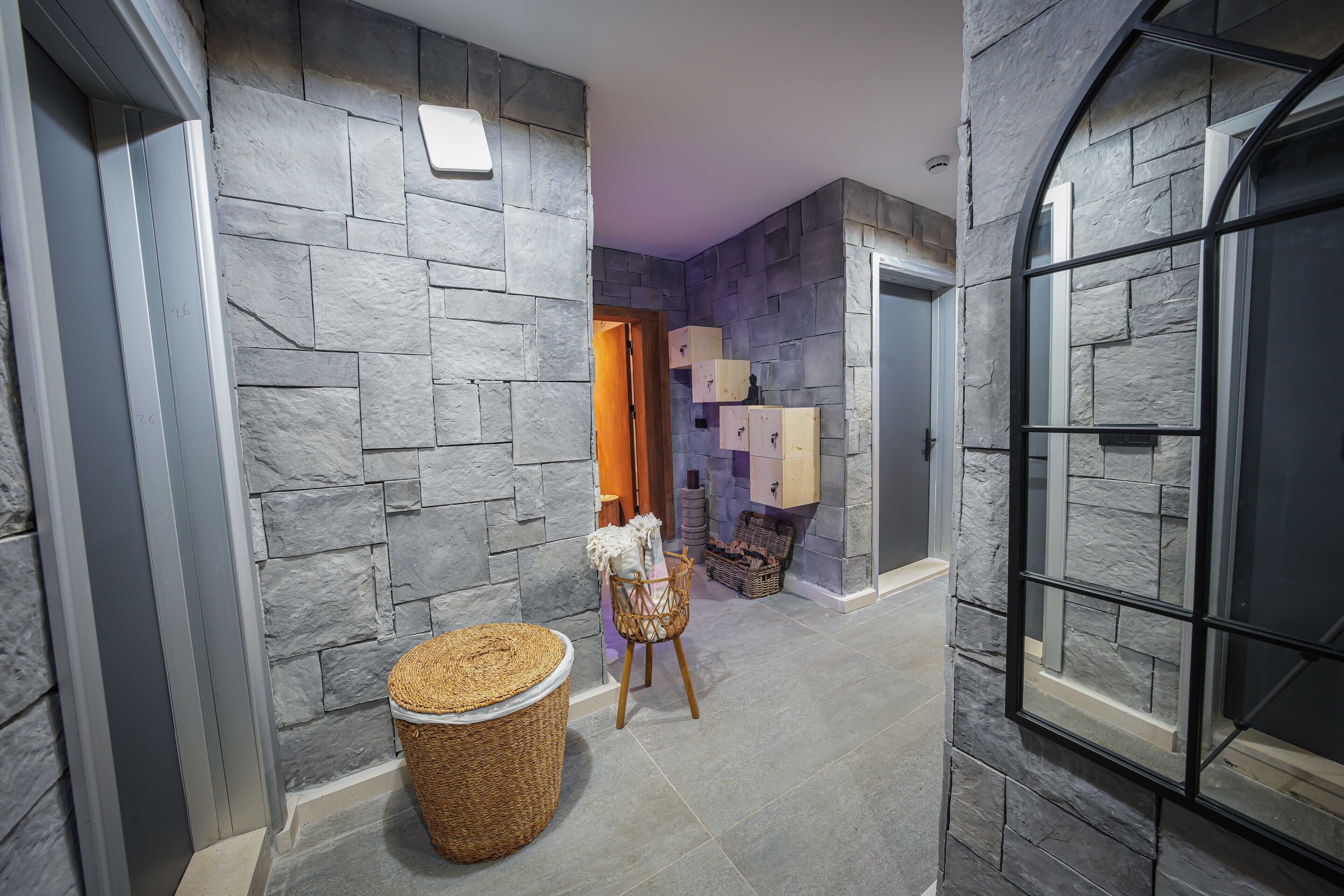 A hallway with stone walls, a wicker basket, a chair, and a wooden door.