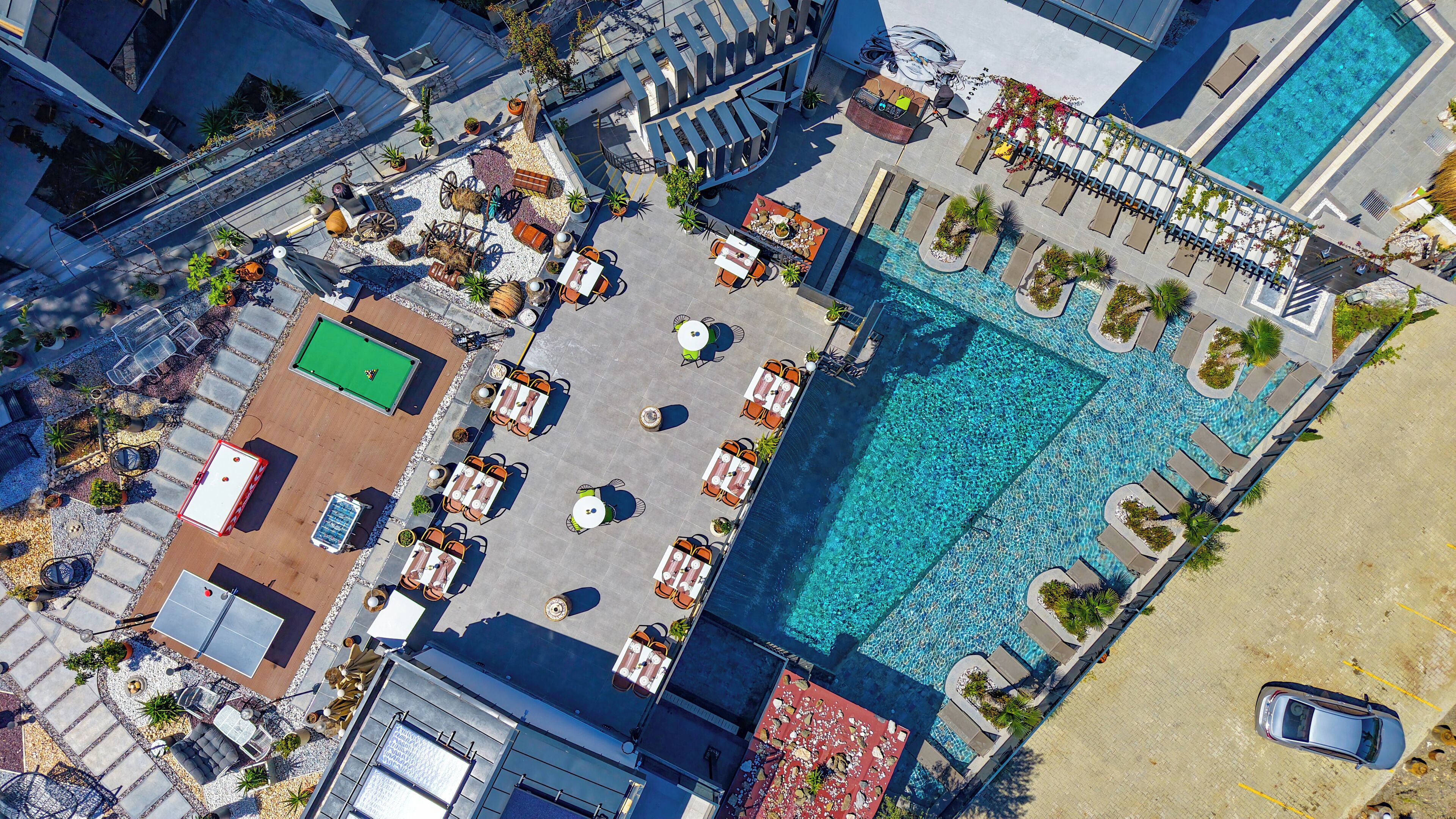 An aerial view of a resort with a swimming pool, outdoor seating areas, and a tennis court.