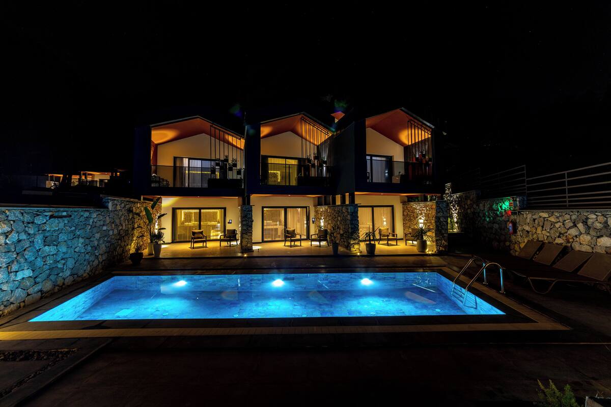 A modern two-story house with a swimming pool in front, stone walls, and outdoor seating.