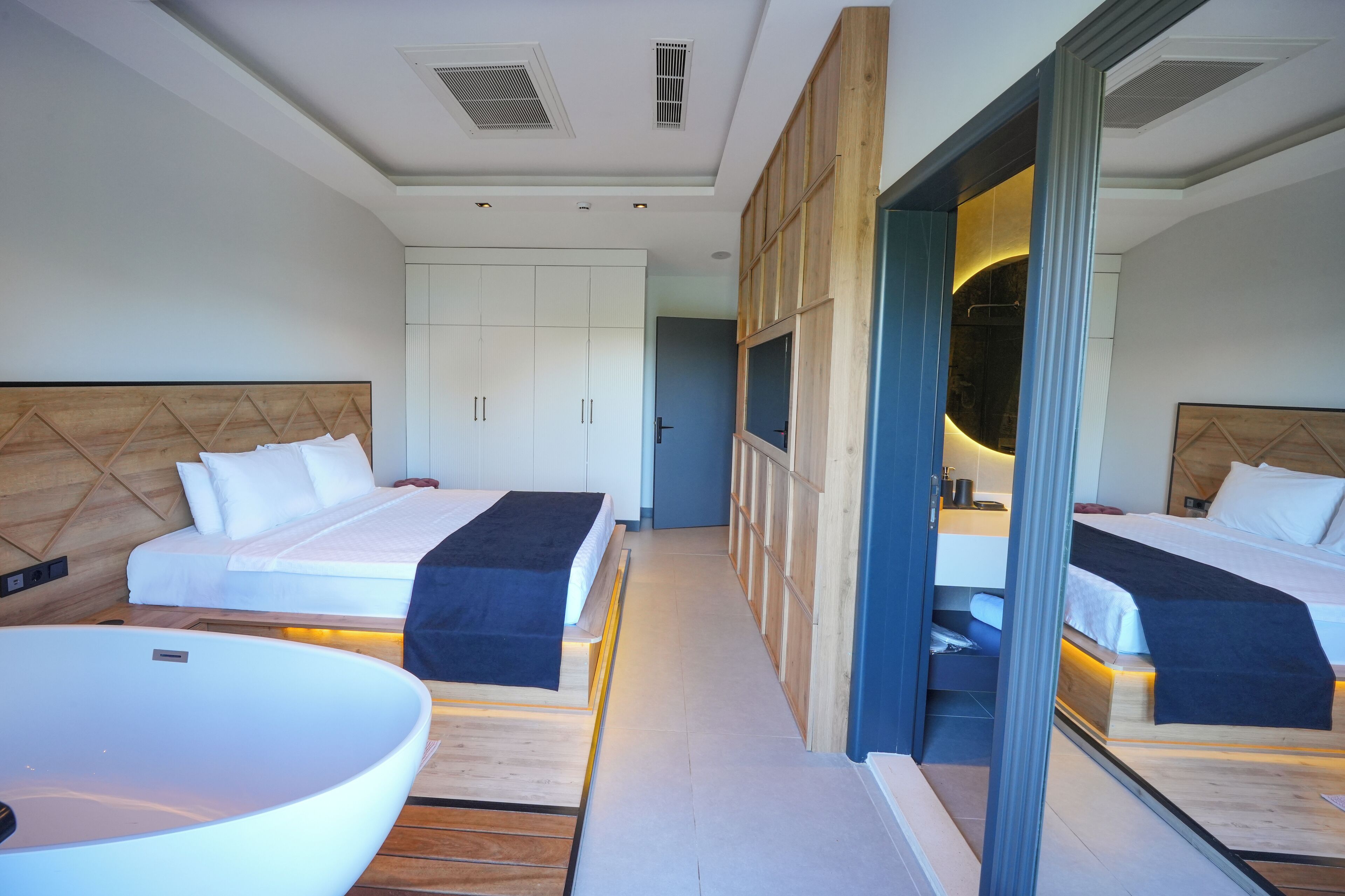A modern hotel room with two beds, a large white bathtub, and a wooden headboard.