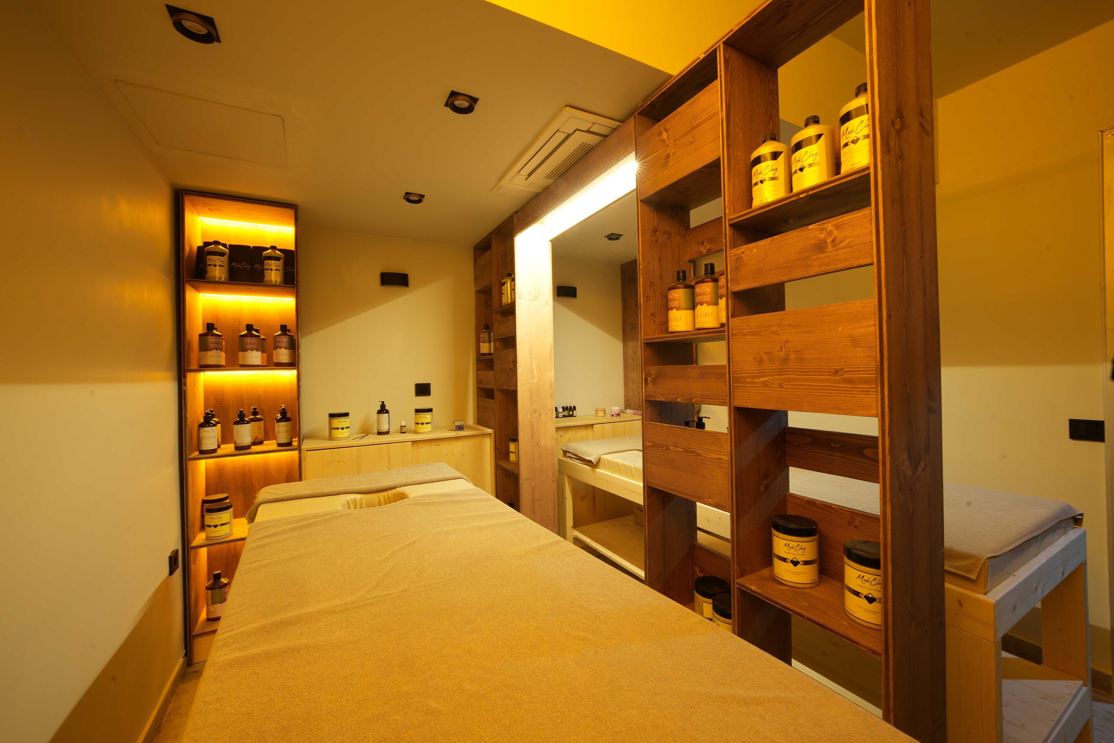 A hotel room with a bed, wooden shelves with bottles, a mirror, and a small desk.