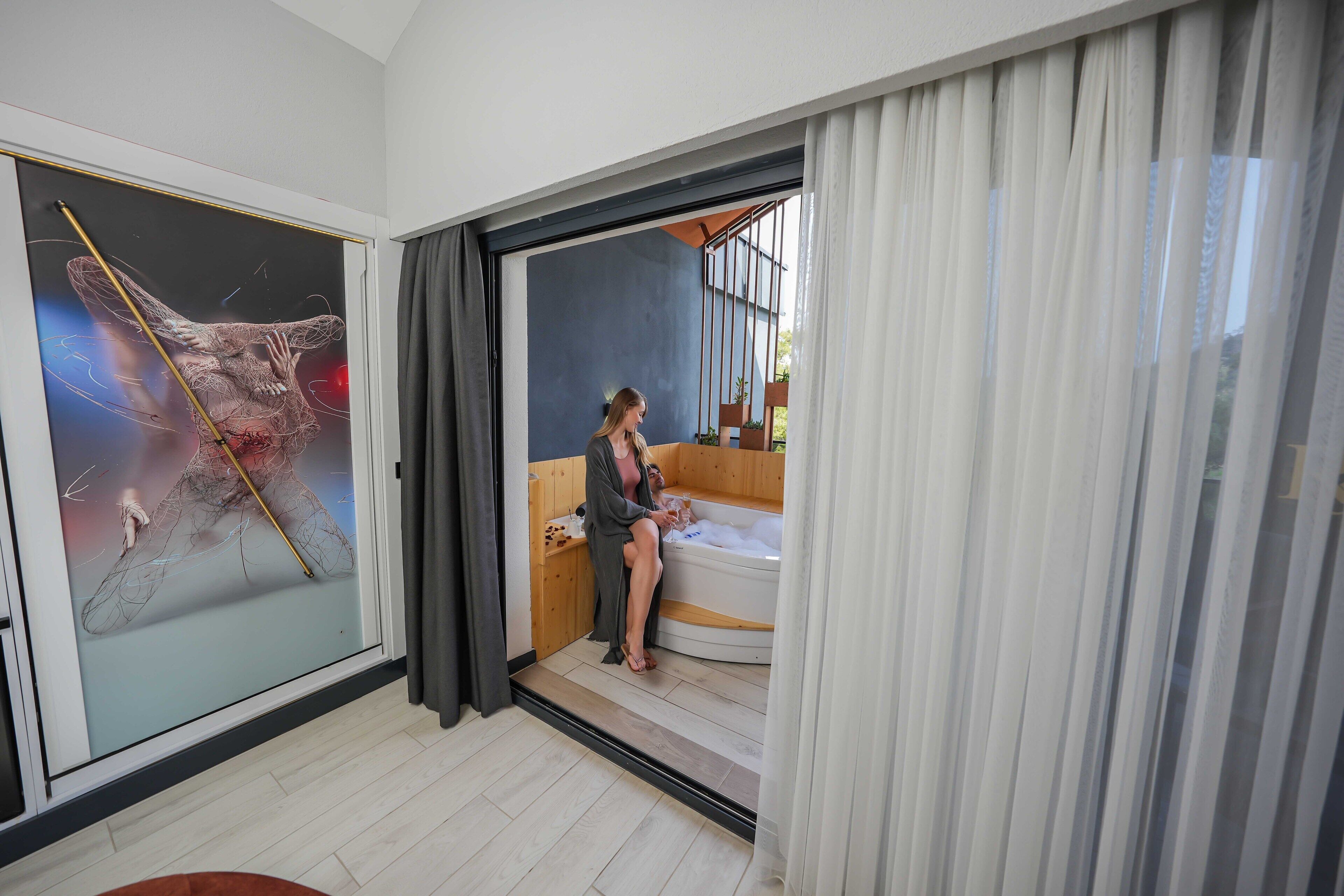 A modern bathroom with a glass shower enclosure, a bathtub, and a large artwork on the wall.