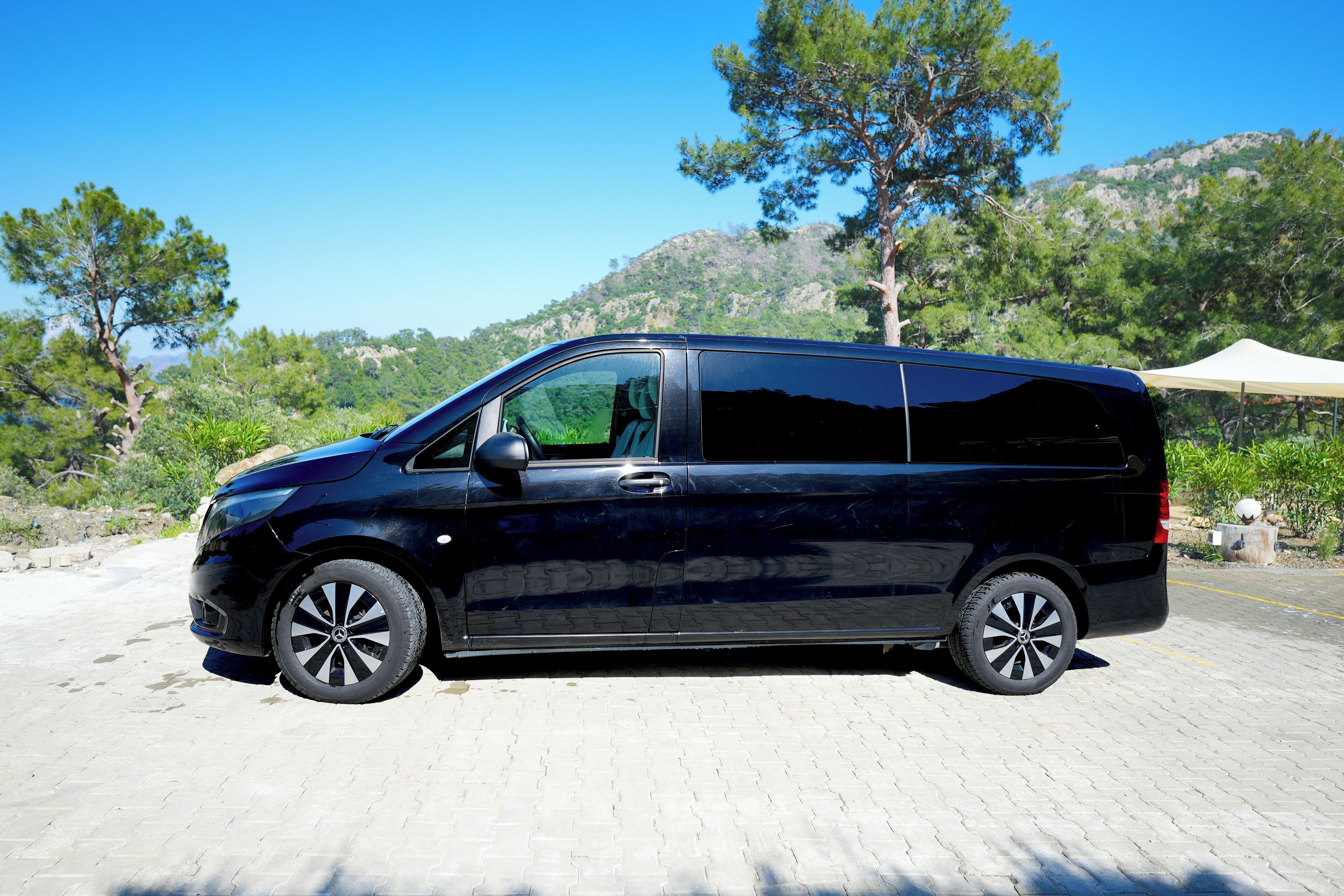 A black van parked on a paved area with a mountainous backdrop and trees.