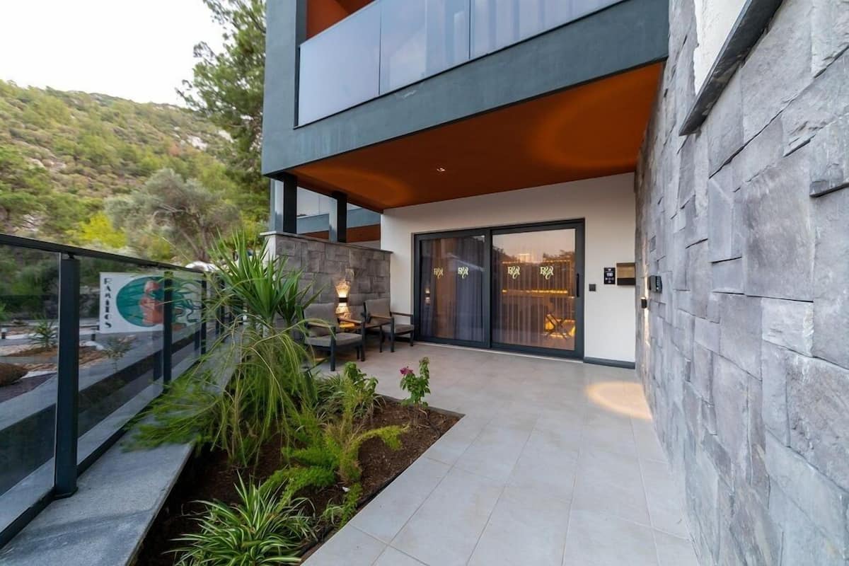 A modern building with a stone facade, a covered patio area with seating, and a view of a mountainous landscape.