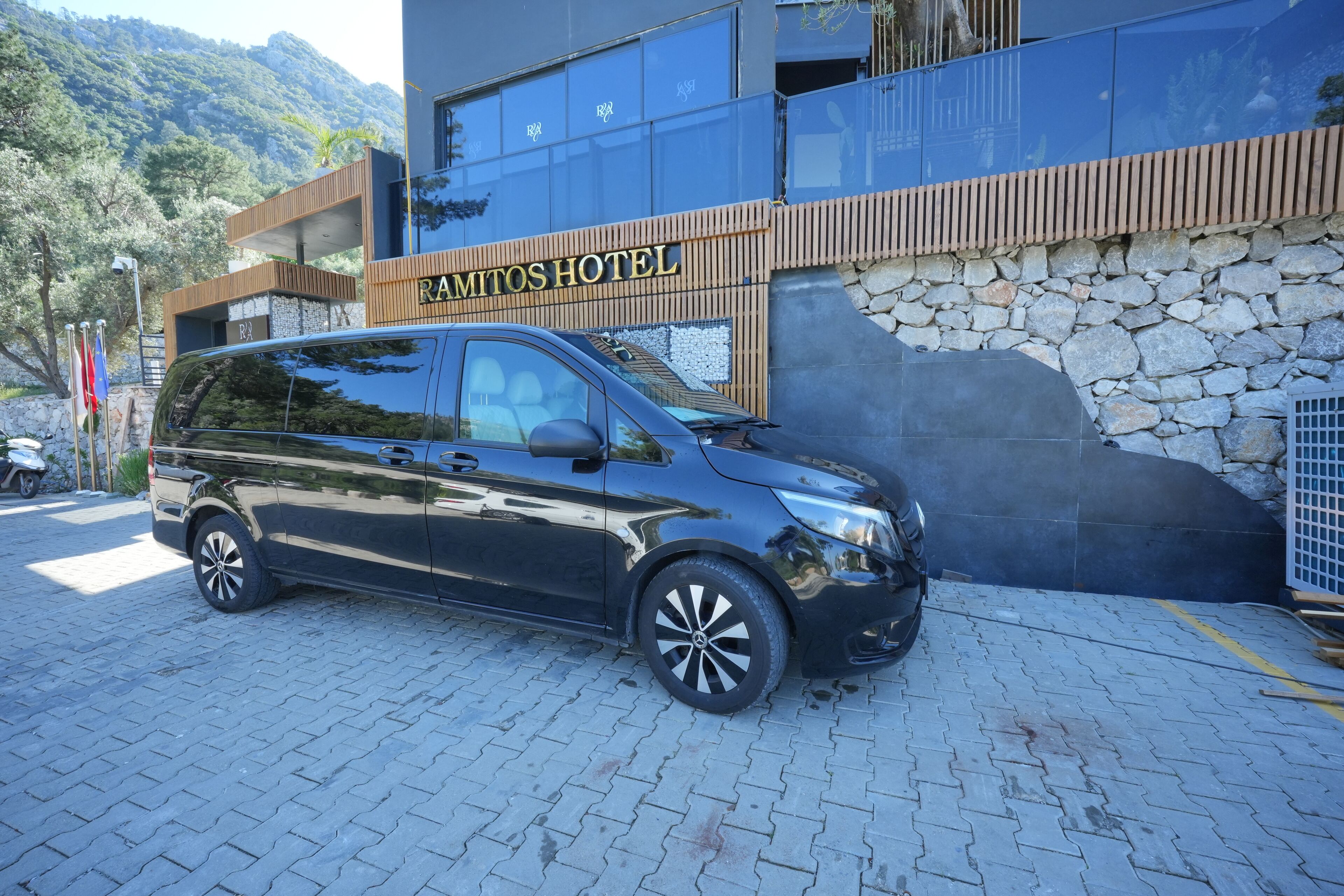 A black minivan parked in front of Ramitos Hotel, which features a stone facade and wooden accents.