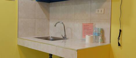 A small kitchenette with a sink, a blue cabinet, a fan, and a sign with a list of amenities.