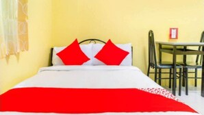 A bed with a red and white bedspread, two red pillows, and a white headboard. There is a small table with chairs to the right of the bed. - Yellow Pad Hotel Davao (Davao)