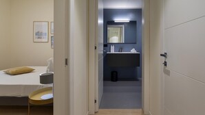 A hotel room with a bed, bedside table, lamp, and a bathroom with a sink and mirror. - Riviera Flavour Apartments by Wonderful Italy - Malva (Santa Margherita Ligure)