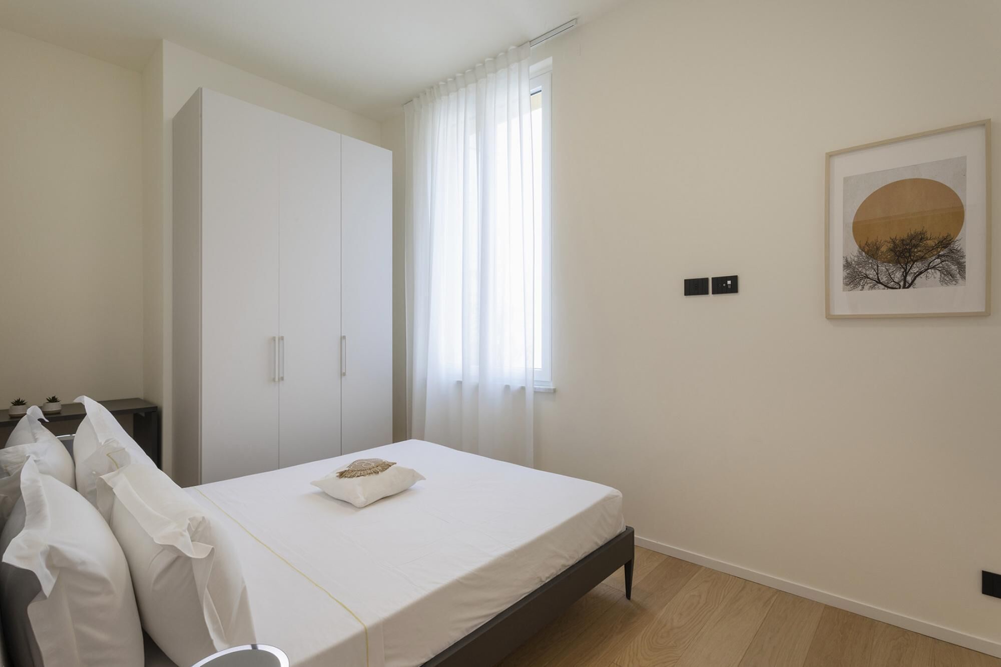 A bedroom with a bed, a wardrobe, a window with curtains, and a framed picture on the wall.