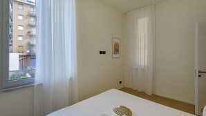 Un dormitorio con cama, una ventana con cortinas, una puerta y un cuadro en la pared.