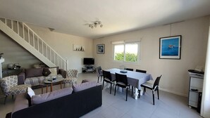 A living room with a staircase, a dining area, and a TV. - Maison pieds dans l'eau St Florent (Saint-Florent)
