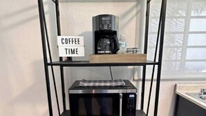 Un coin cuisine équipé d’une machine à café et d’un four à micro-ondes, le tout posé sur une étagère en métal noir.