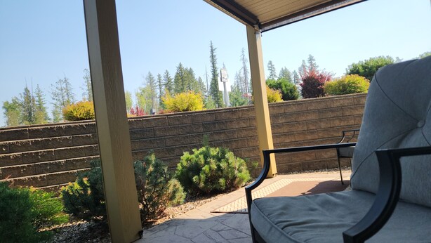 A covered patio area with a stone floor, a bench, and a low stone wall with various plants. - Quiet, forest view condo at Mabel Lake - Dog friendly! (Enderby)
