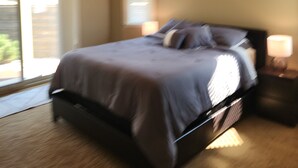 A bedroom with a bed, a ceiling fan, a nightstand with a lamp, and a view of the outdoors through a window. - Quiet, forest view condo at Mabel Lake - Dog friendly! (Enderby)