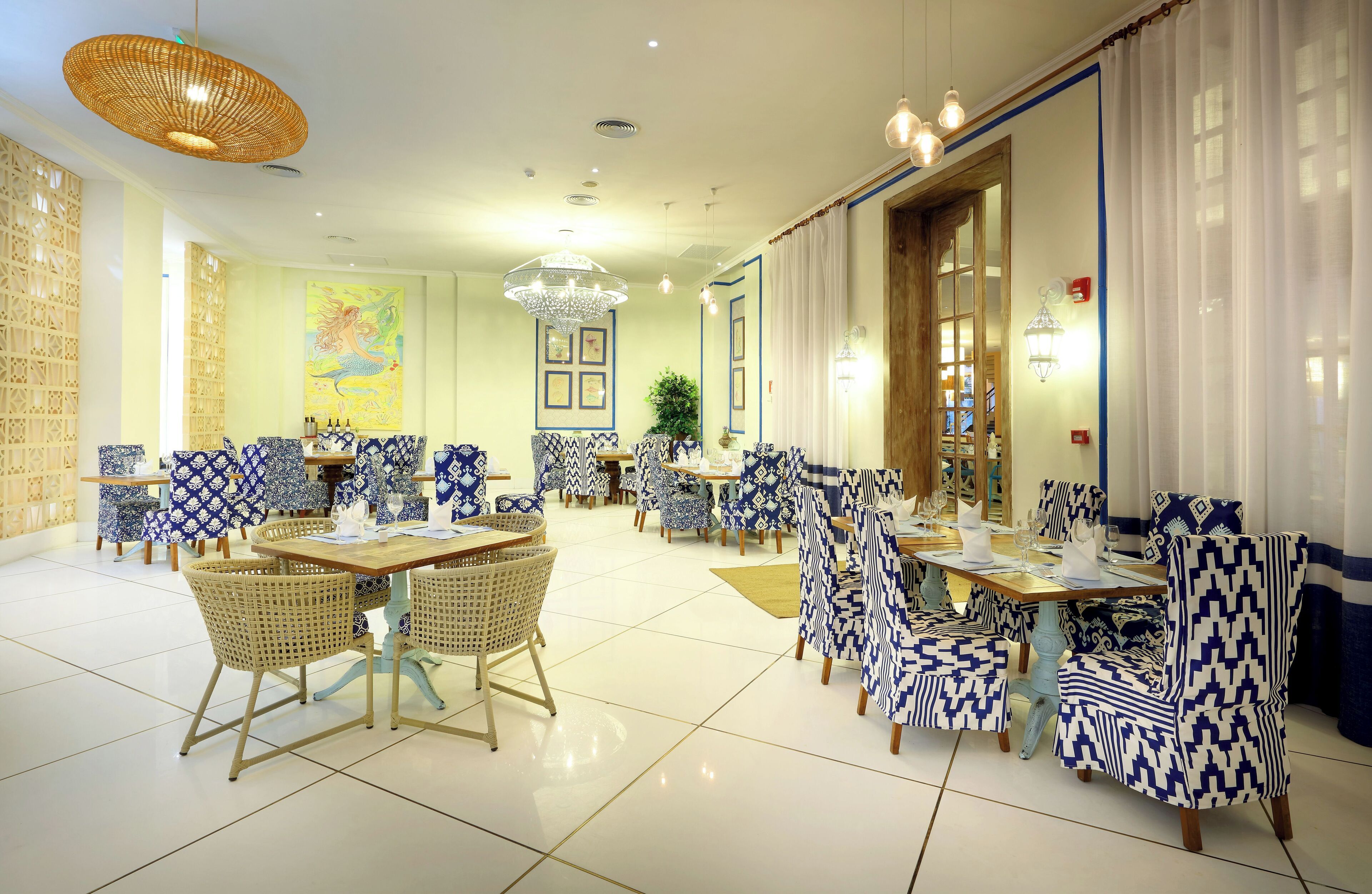 A spacious dining area with blue and white patterned furniture, a large chandelier, and a decorative wall painting.