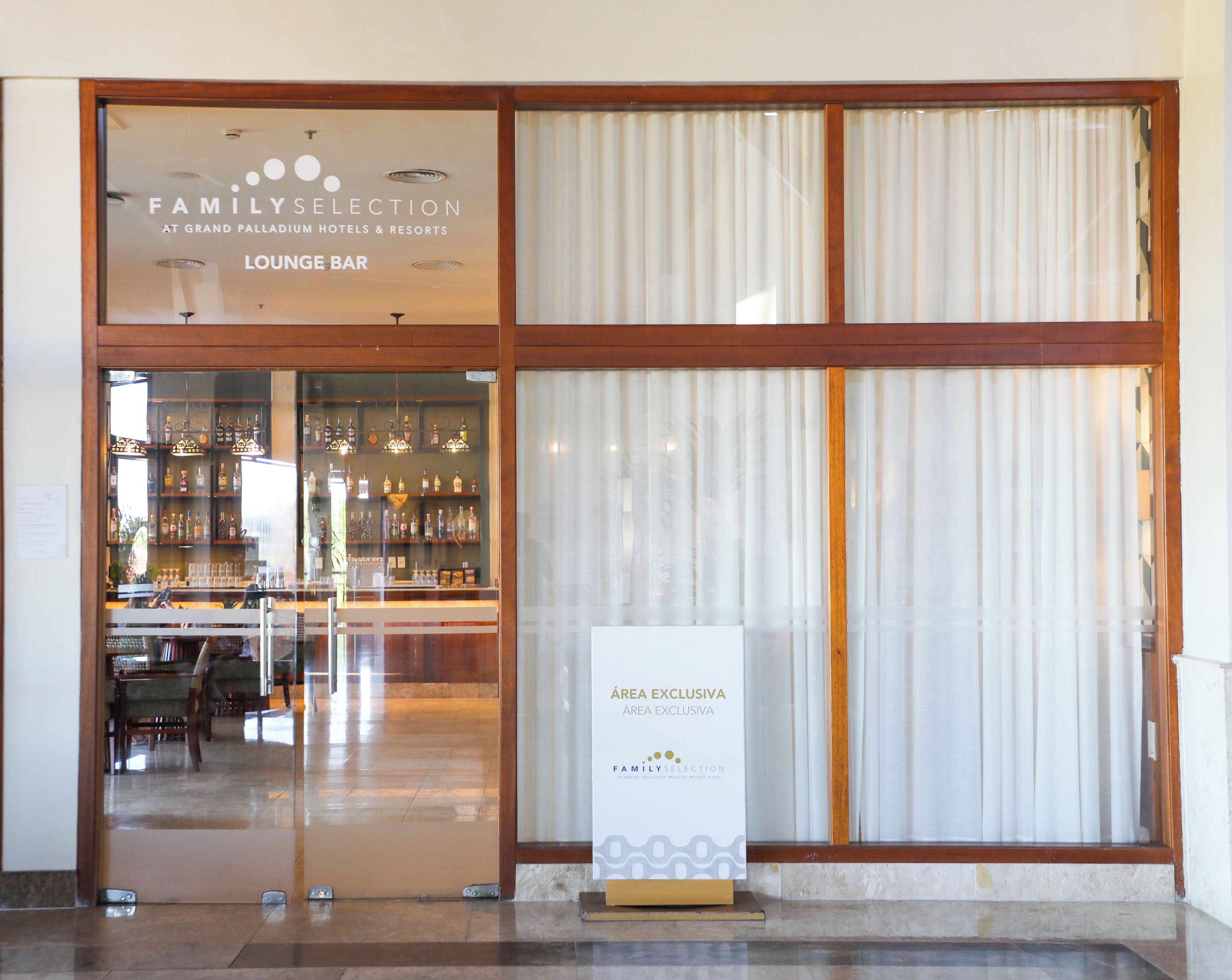 A lounge bar with a glass front, a sign indicating an exclusive area, and a bar stocked with bottles.