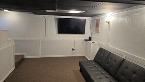 Una sala home theater con un grande televisore piatto montato a parete, un divano in pelle nera e un pavimento rivestito di moquette.