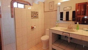 A bathroom with a white toilet, a sink with a mirror, and a shower area. - 2bdup Casalaspalmas Puntademita (Punta de Mita)